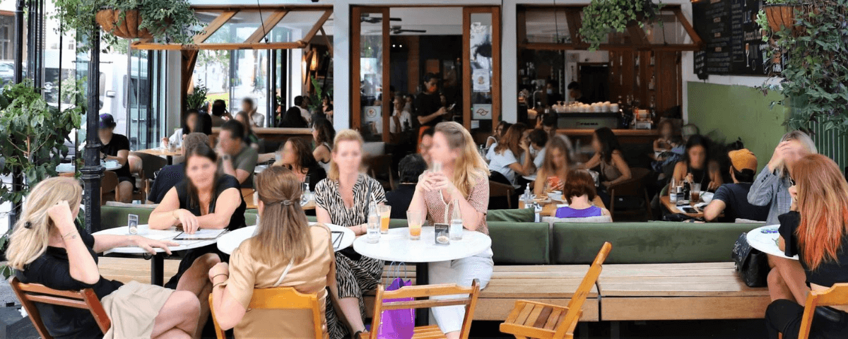 Unidade da Cafeteria Santo Grão da Oscar Freire, com a área externa cheia de pessoas nas mesas. A cafeteria possui diversos cafés especiais e é perfeita para celebrar o Dia Mundial do Café. 