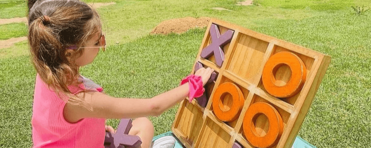 Menina sentada em um gramado brincando de jogo da velha. 