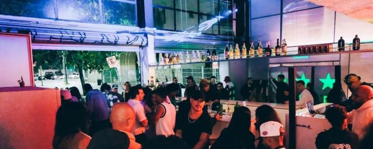 Diversas pessoas no ambiente do House of Coisas, que é aberto e integrado com a rua. 