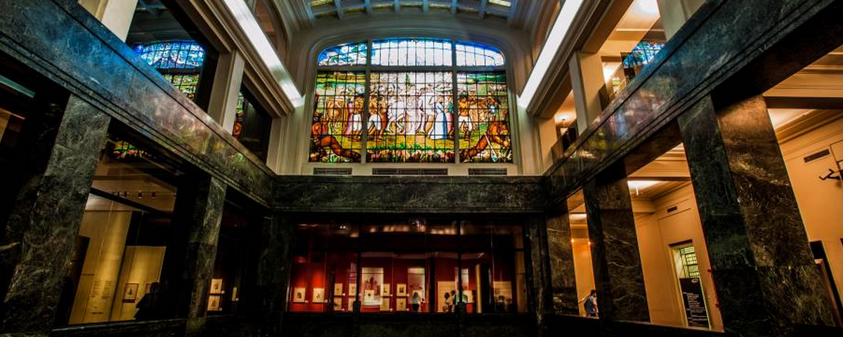 Vitrais coloridos em um ambiente com colunas de mármore, dentro da Caixa Cultural.