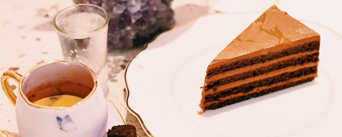 Pedaço de torta com camadas de chocolate e doce de leite e uma xícara com café ao lado. 