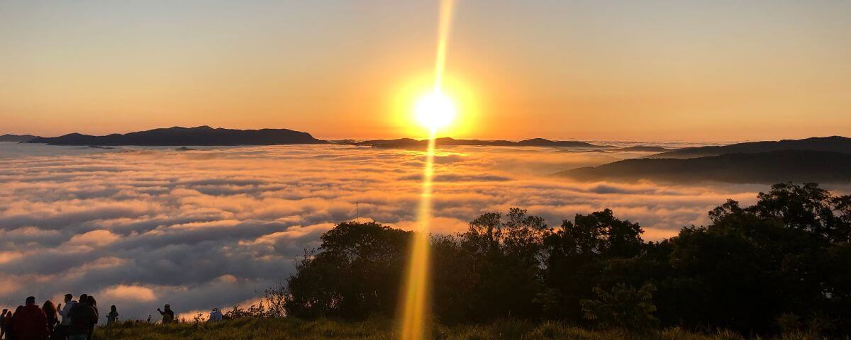 Pôr do sol com nuvens cobrindo as montanhas no Pico do Olho D'Água.  