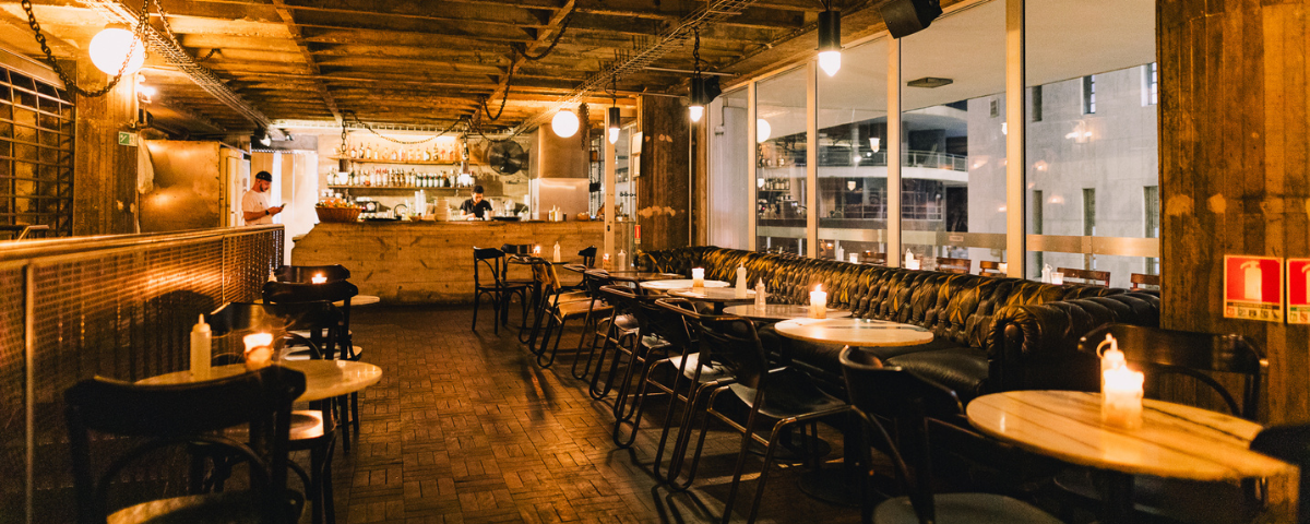 Ambiente do bar Orfeu, que faz parte das opções de norte a sul, possui luz baixa e cadeiras na cor preta. 