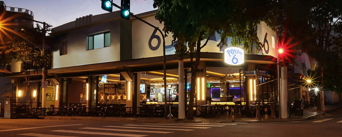 Fachada do bar Posto 6, que fica em uma esquina, com diversas mesas e cadeiras.