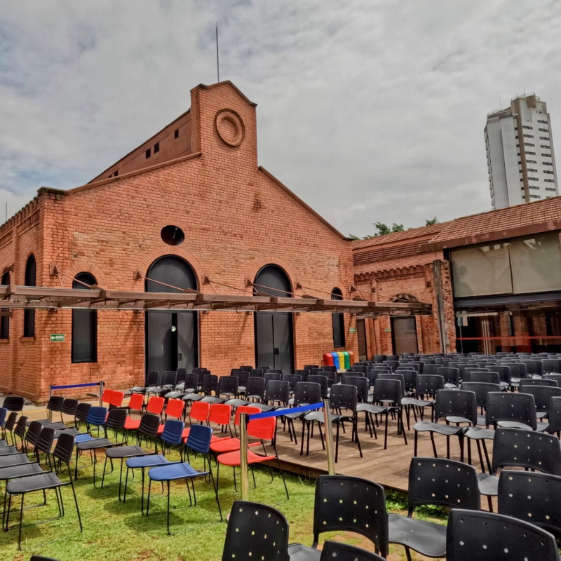 A imagem mostra a área externa do gramado com cadeiras do cinema ao ar livre da Cinemateca Brasileira