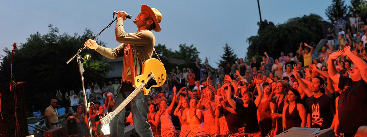 A imagem mostra o artista Ben Harper contando e ao fundo os telespectadores