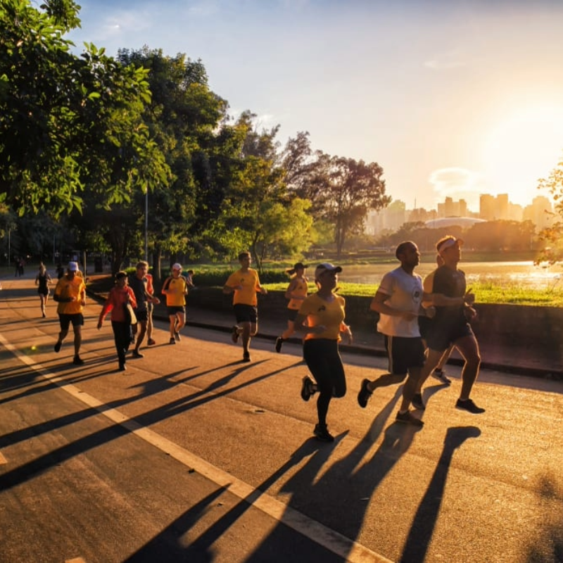 A imagem mostra os corredores no Parque Ibirapuera e ao fundo o lago com o por do sol