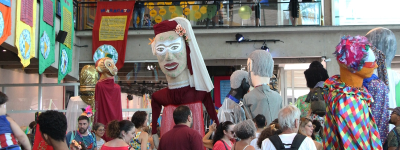 Visitantes no interior do Sesc Santo Amaro durante o Carnaval com bonecos fantasiados.