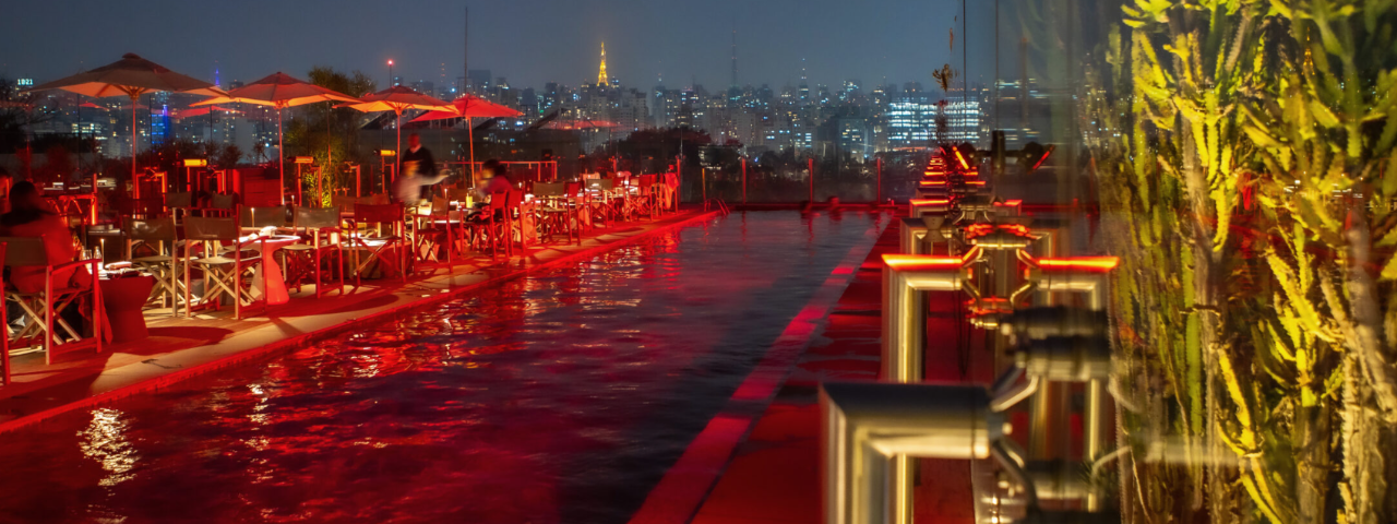 Imagem noturna da piscina vermelha do Skye Bar e a cidade de SP ao fundo