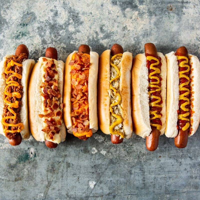 Diversos hot dogs servidos em fila, prontos para serem degustados, representando opções populares em São Paulo