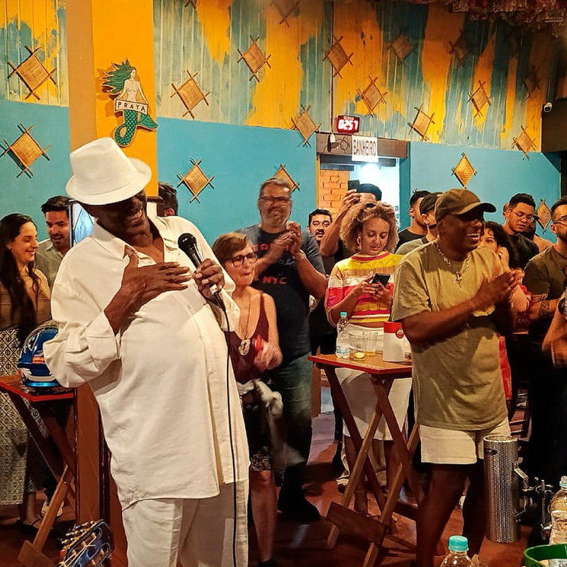 Cantor animando uma roda de samba com pessoas ao redor curtindo o som contagiante