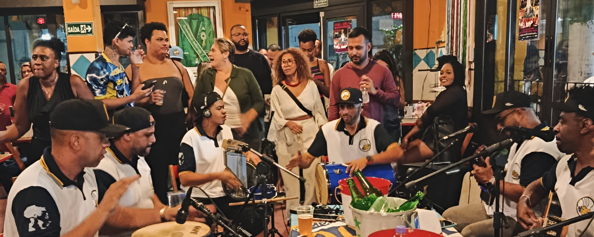 Grupo de samba tocando em uma roda, com pessoas ao redor aproveitando o clima descontraído