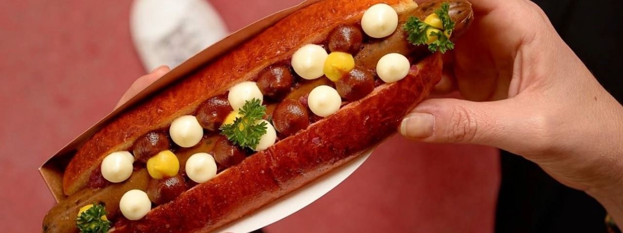 Mãos segurando um hot dog do Hot Pork, capturando o momento de apreciação de um dos melhores hot dogs artesanais de São Paulo
