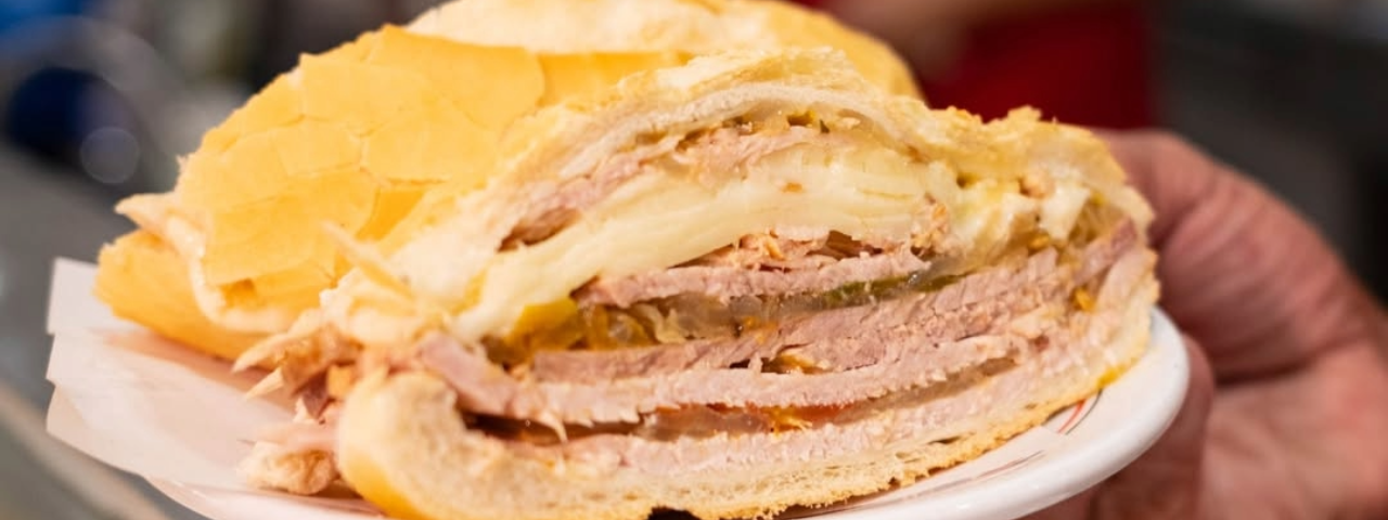 Mão segurando um prato com um suculento sanduíche de pernil, destaque para quem aprecia um sabor autêntico em São Paulo