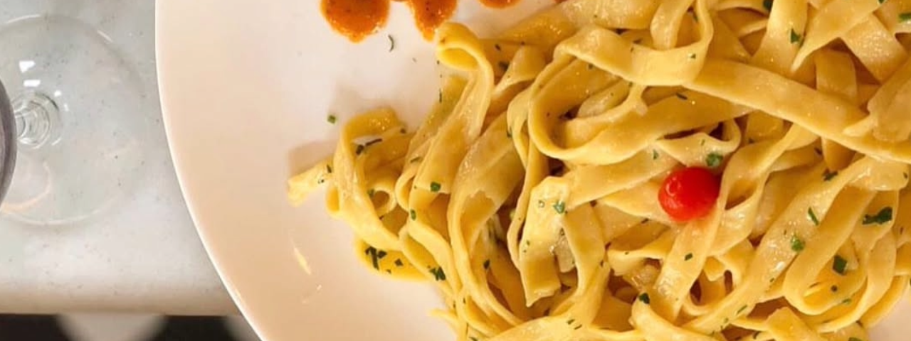Prato de macarrão finalizado com tempero verde e pimenta biquinho, realçando o sabor e a cor