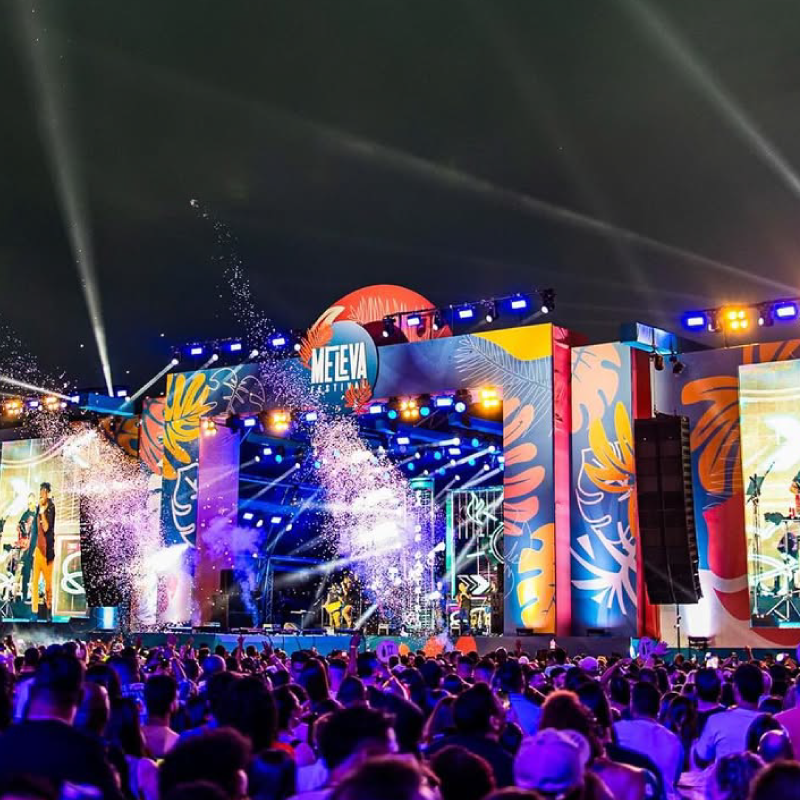 Evento Me Leva Festival, com pessoas assistindo ao show e uma banda se apresentando ao fundo no palco principal