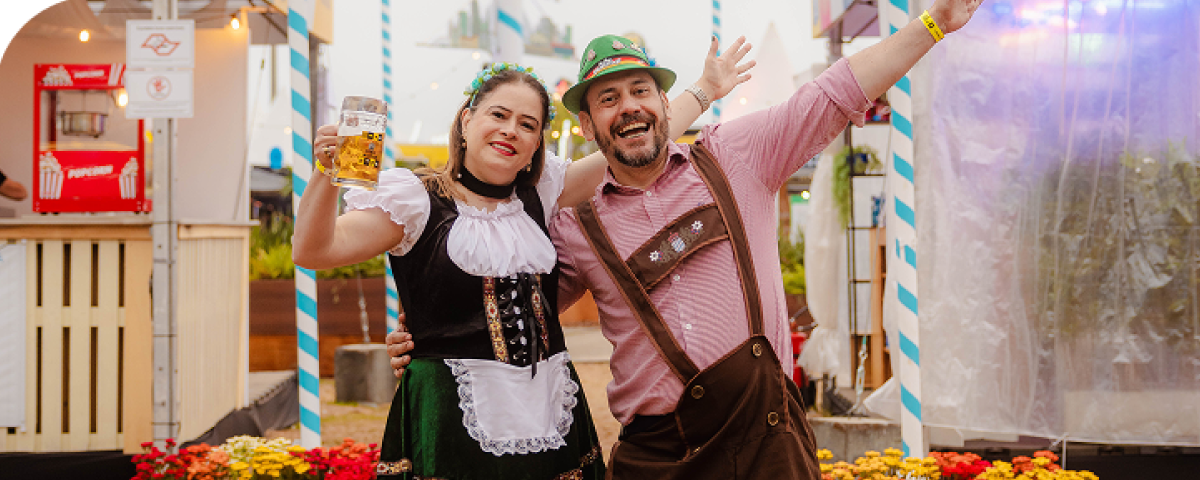 Casal alegre curtindo o festival Oktoberfest, com roupas típicas e canecos de cerveja