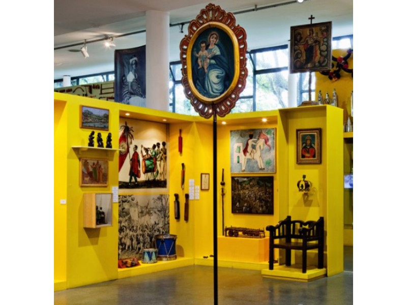 imagem mostra exposição do Museu Afro Brasil com uma estante amarela e objetos históricos