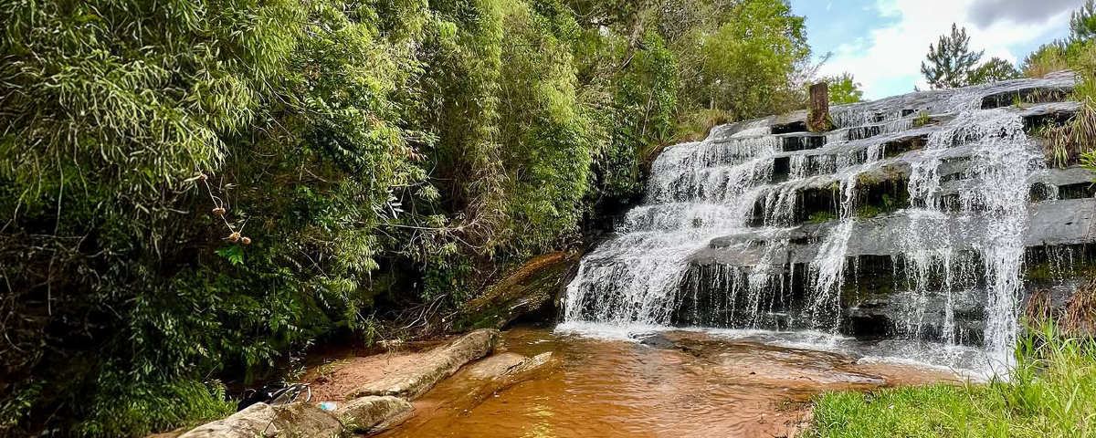 Queda d'água de uma cachoeira em meio à vegetação, formando um cenário ideal para ecoturismo