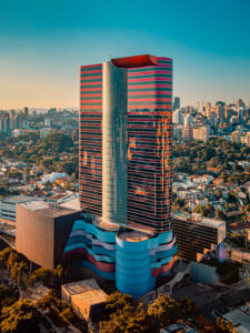 imagem mostra vista aérea de edifício espelhado com listras azuis e rosas com cidade ao redor