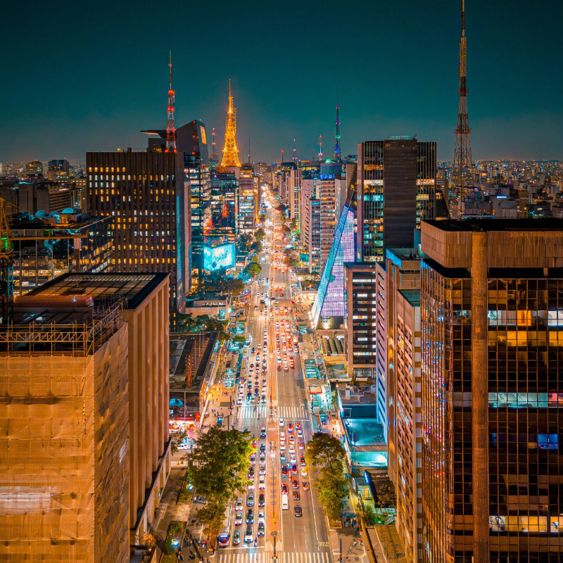 Vista aérea da Avenida Paulista à noite, iluminada pelos prédios e movimentada com luzes dos carros