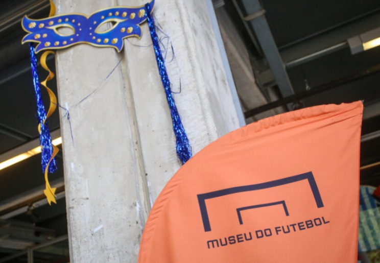 foto mostra banner do museu do futebol e mascara azul de carnaval