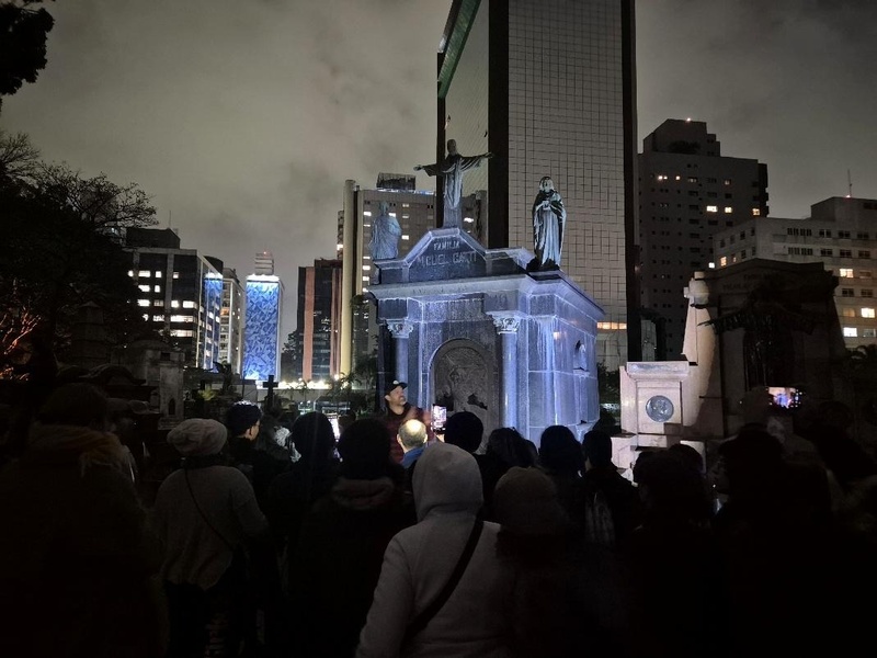 foto mostra pessoas a note em frente a uma cripta
