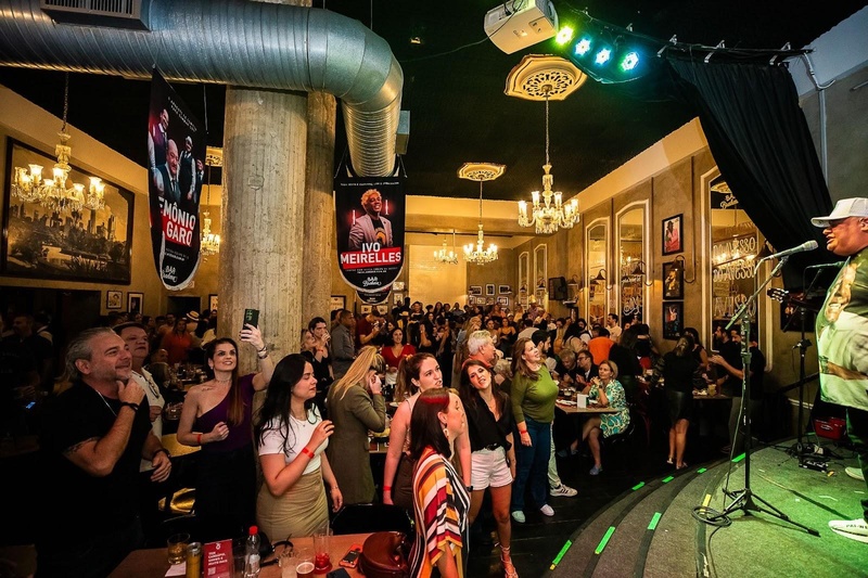 imagem mostra pessoas se divertindo em um bar com musica ao vivo