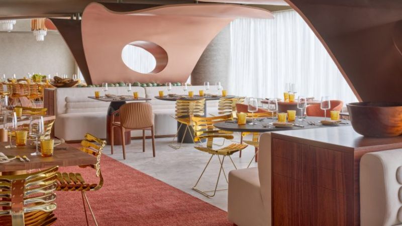Interior do restaurante Baio, no W São Paulo, com decoração contemporânea em tons terrosos, mesas postas para brunch e cadeiras douradas em ambiente sofisticado e iluminado.
