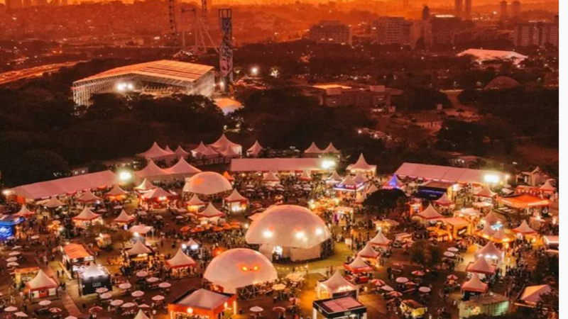 Vista aérea noturna do Taste São Paulo Festival mostra estrutura do evento com tendas, domos iluminados, restaurantes e grande circulação de público ao ar livre.