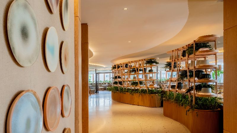 Interior do restaurante Quint.e, no The Westin São Paulo, com decoração contemporânea em madeira clara, prateleiras com plantas e ambiente sofisticado e iluminado.