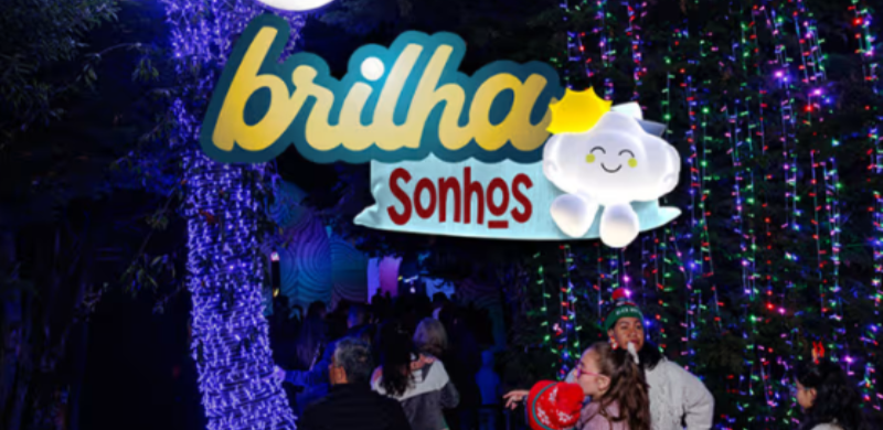 Entrada do Festival Brilha Sonhos no Parque Villa-Lobos durante a noite. Um letreiro iluminado com o nome do evento está instalado entre árvores decoradas com luzes coloridas, enquanto visitantes caminham pelo percurso de experiências imersivas ao ar livre.