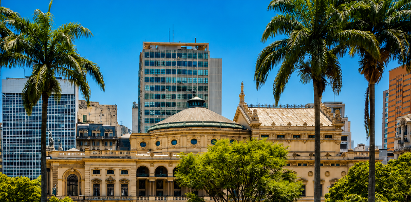 Dia do Cinema Brasileiro: vista do Theatro Municipal de São Paulo. A imagem mostra o edifício histórico cercado por jardins e palmeiras, com prédios da região central da cidade ao fundo.