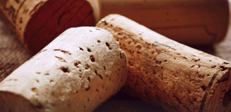 Close em rolhas de cortiça utilizadas em garrafas de vinho, apoiadas sobre uma superfície de tecido. Ao fundo, uma garrafa e outra rolha desfocadas reforçam a imagem como símbolo da produção vinícola e das experiências de enoturismo em São Paulo.
