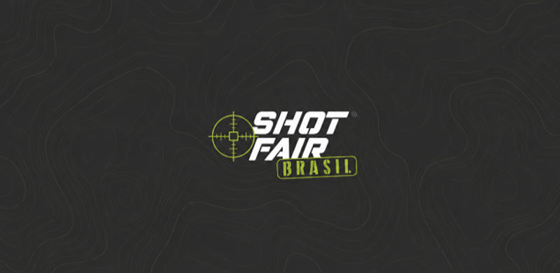 Arte gráfica com fundo preto texturizado por linhas topográficas em tons de cinza. No centro inferior, aparece o logotipo da Shot Fair Brasil em branco e verde-limão, composto por uma mira estilizada ao lado do nome "Shot Fair" e da palavra "Brasil" em destaque dentro de um retângulo inclinado. Há amplo espaço vazio ao redor do logotipo, valorizando a identidade visual do evento.