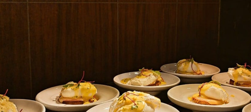 Diversos pratos individuais dispostos no Restaurante Tarsila, com ovos pochê sobre fatias de pão, molho cremoso e brotos frescos.