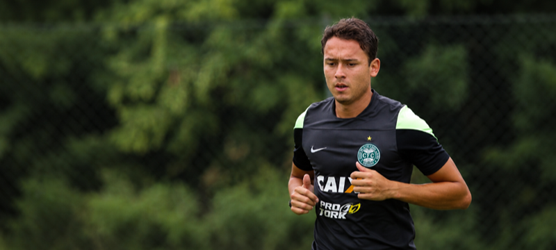 Homem corre durante treinamento em campo de futebol, vestindo uniforme esportivo preto do Coritiba. Ao fundo, árvores e alambrado aparecem desfocados.